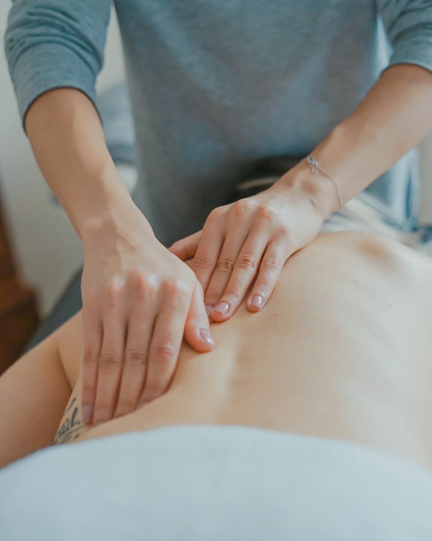 A massage therapist working with both hands along a client's upper back.