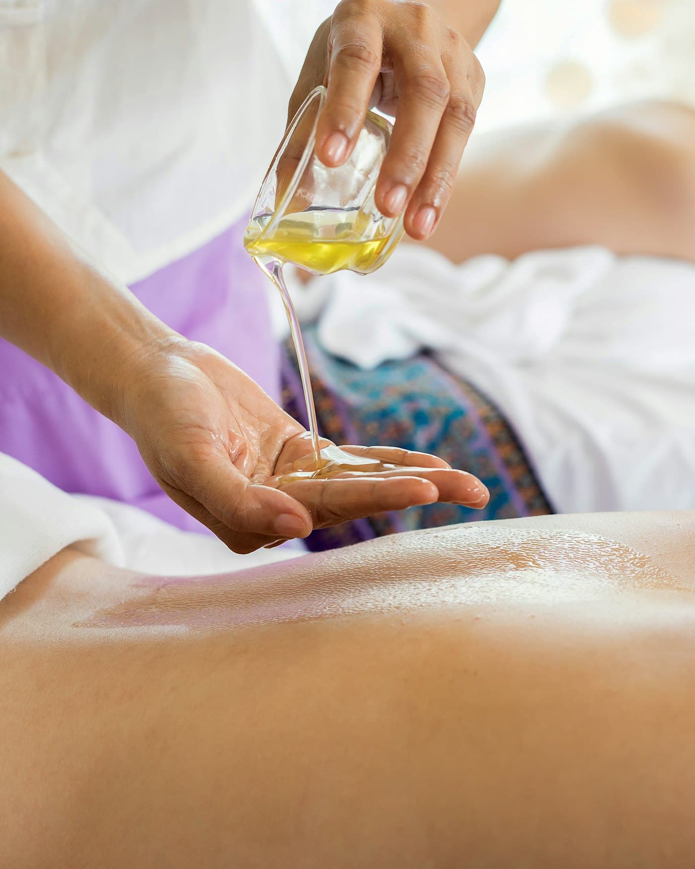 Massage oil being warmed and applied across a client's back.